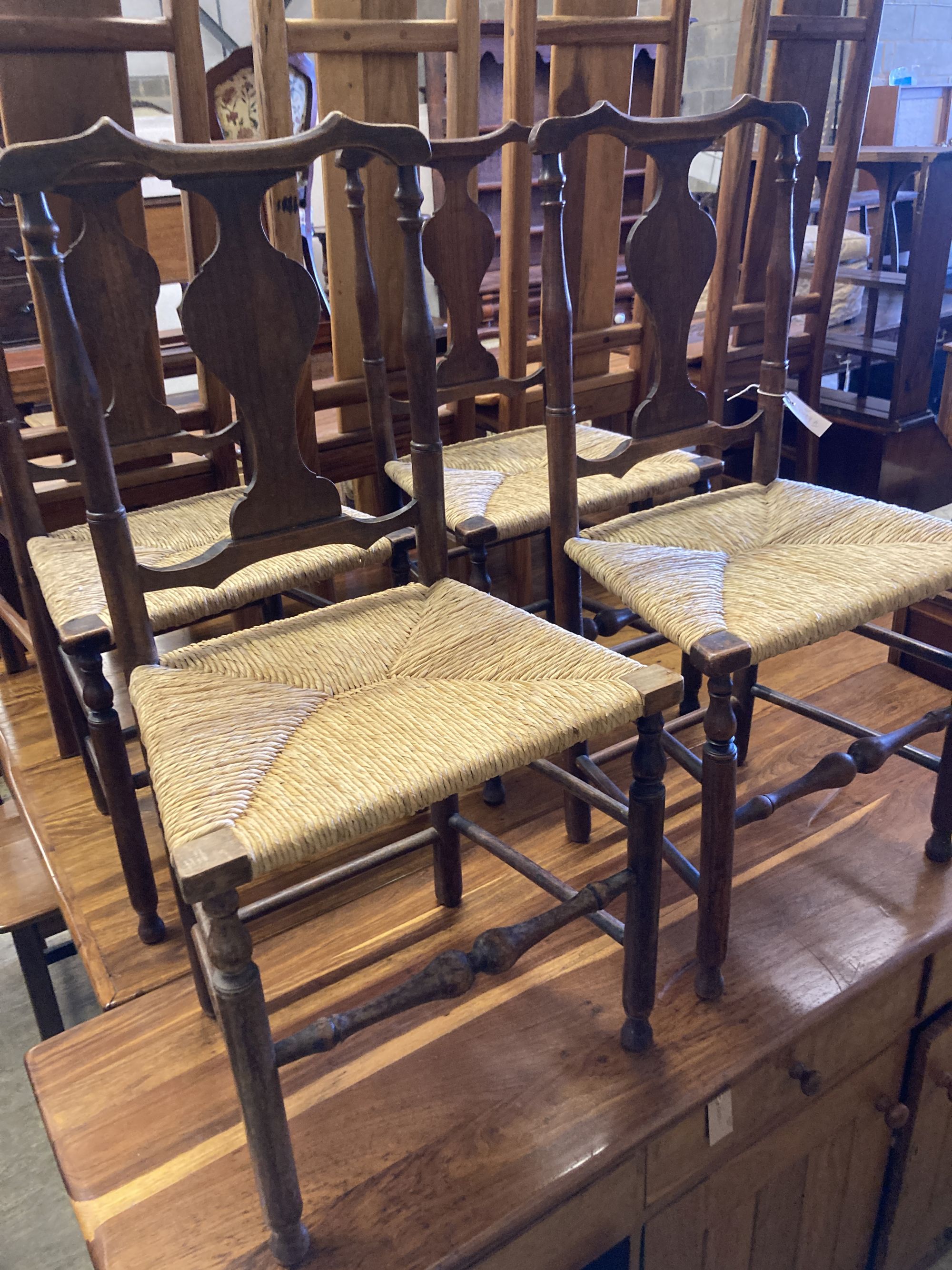 A set of four George III country oak rush seated chairs, with shaped back splat, turned supports and stretchers